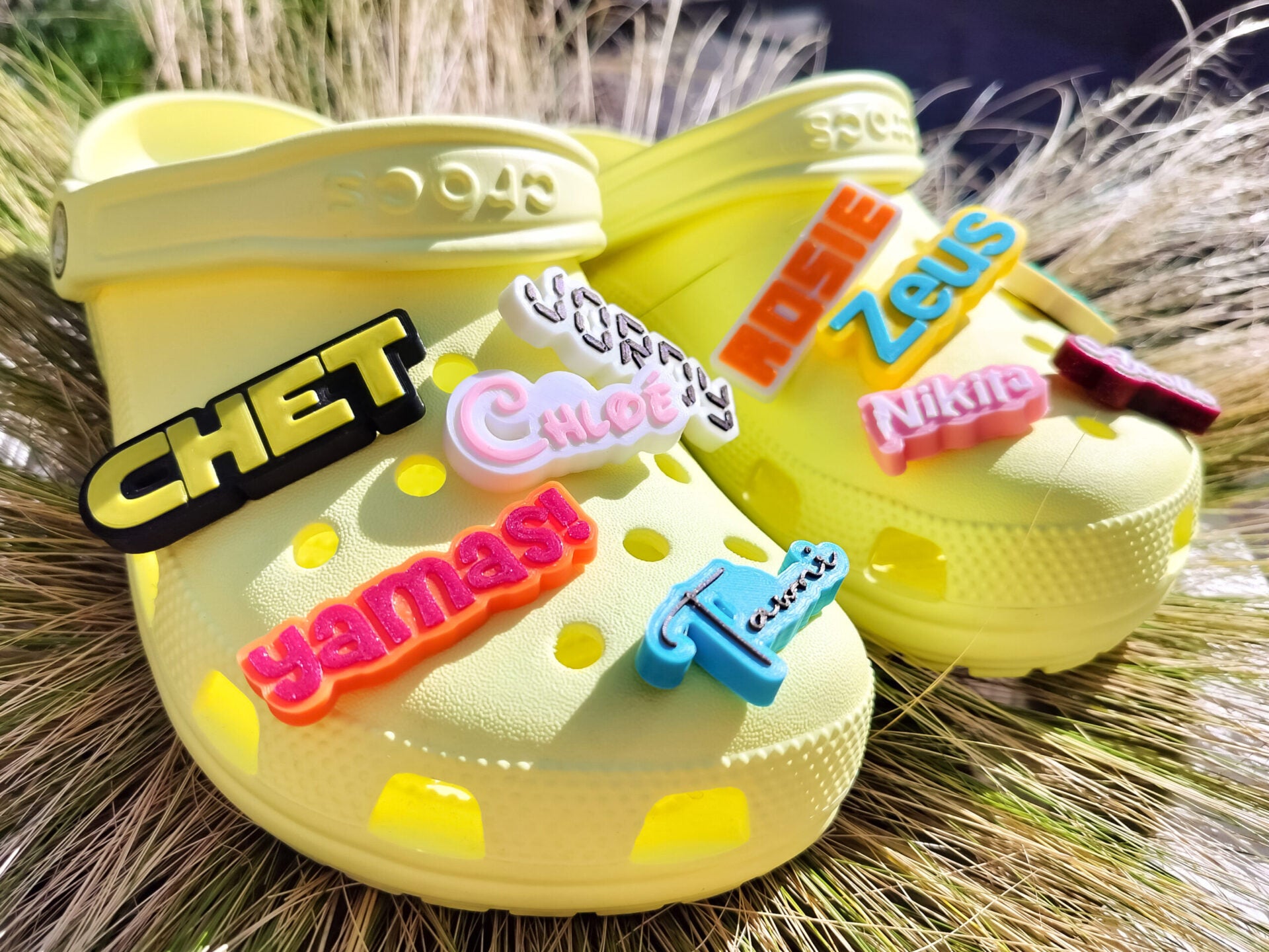 A pair of yellow shoes shoes featuring a variety of colorful, custom name charms. Each charm showcases different names in unique fonts. They allow you to personalize names or phrases with chosen colors and fonts, making each design unique.