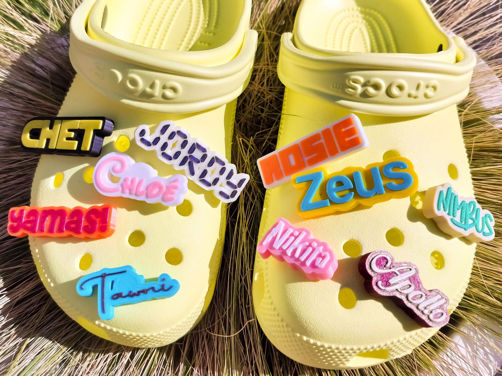 A pair of yellow shoes shoes featuring a variety of colorful, custom name charms. Each charm showcases different names in unique fonts. They allow you to personalize names or phrases with chosen colors and fonts, making each design unique.