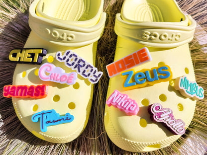 A pair of yellow shoes shoes featuring a variety of colorful, custom name charms. Each charm showcases different names in unique fonts. They allow you to personalize names or phrases with chosen colors and fonts, making each design unique.
