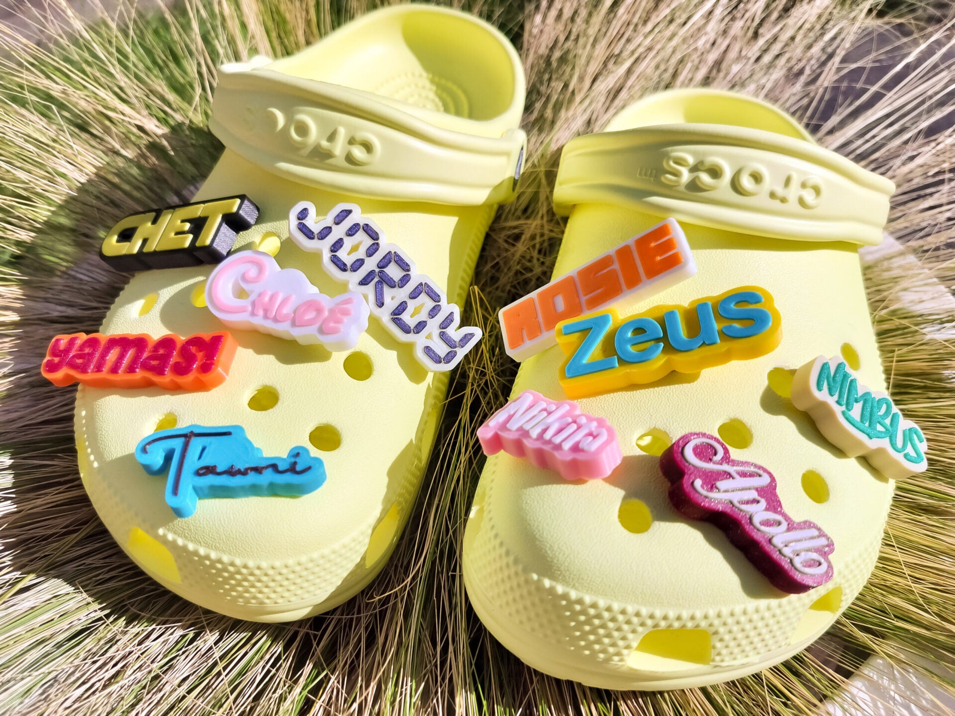 A pair of yellow shoes shoes featuring a variety of colorful, custom name charms. Each charm showcases different names in unique fonts. They allow you to personalize names or phrases with chosen colors and fonts, making each design unique.