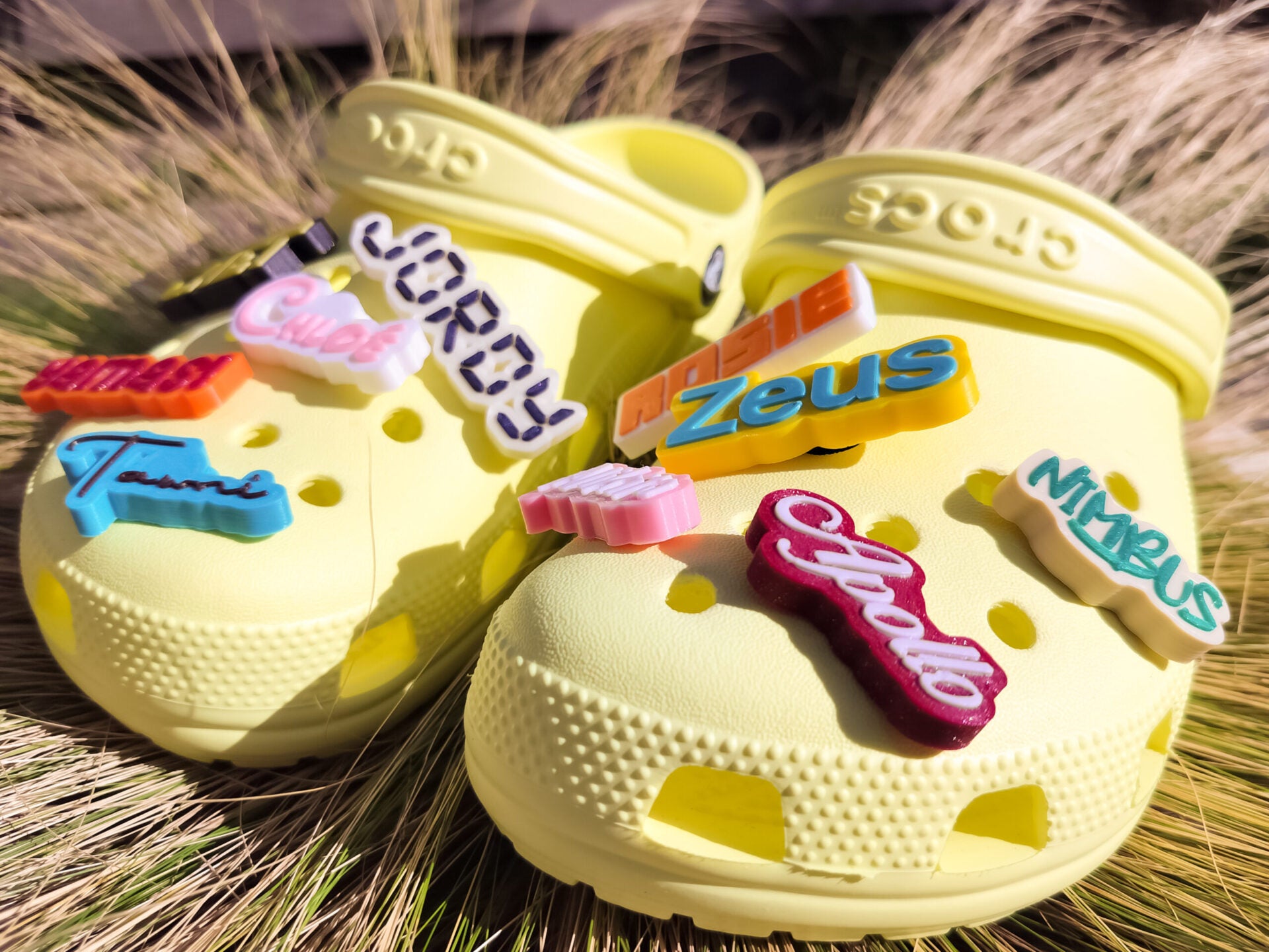 A pair of yellow shoes shoes featuring a variety of colorful, custom name charms. Each charm showcases different names in unique fonts. They allow you to personalize names or phrases with chosen colors and fonts, making each design unique.