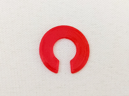 Close-up of a red 3D printed TPU shoe charm Clip designed to secure charms from falling out. The clip is flexible and fits onto the back of charms, fastening them securely to the inside of shoes shoes for added protection during wear.
