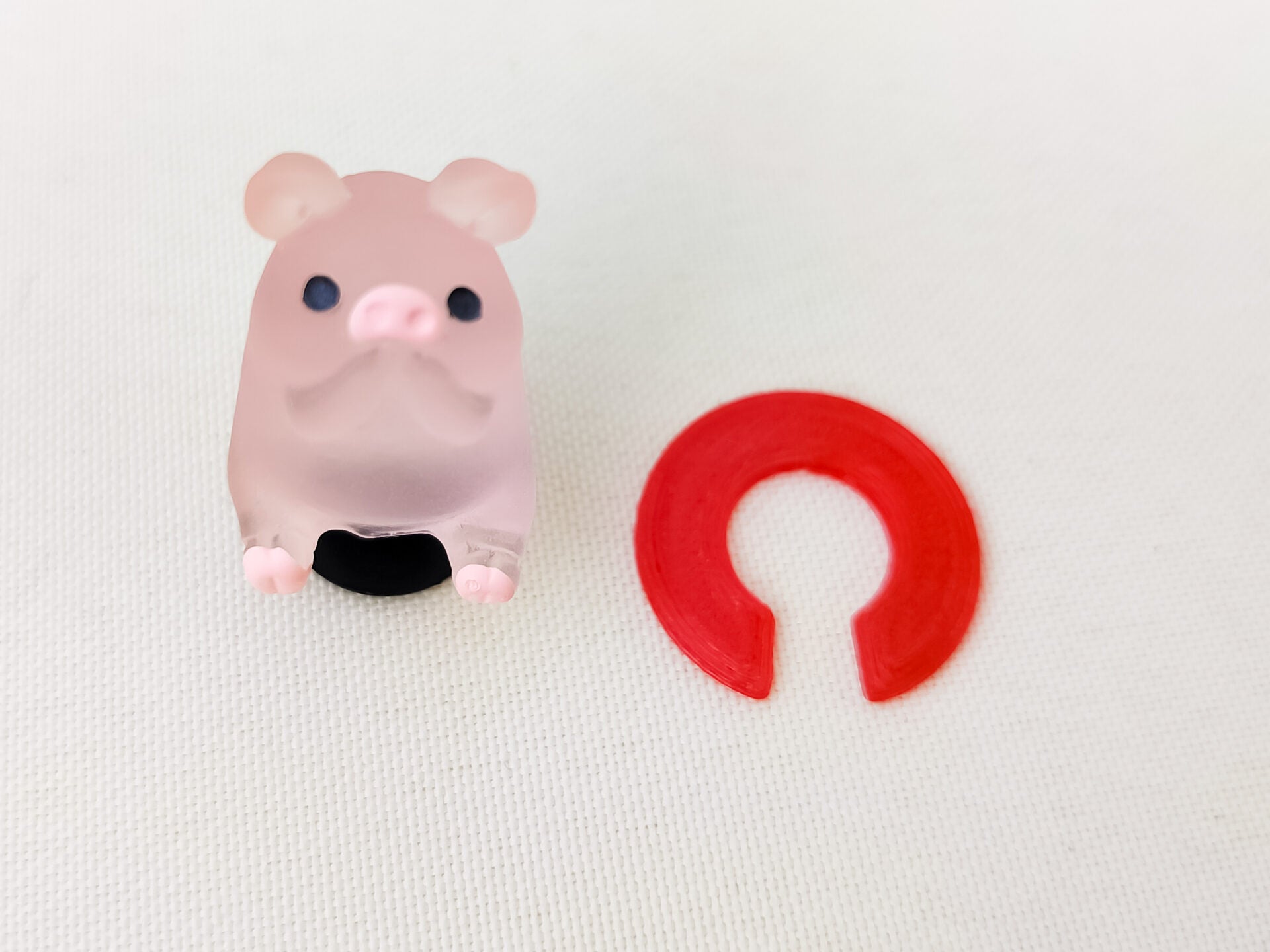 Close-up of a red 3D printed TPU shoe charm Clip designed to secure charms from falling out. The clip is flexible and fits onto the back of charms, fastening them securely to the inside of shoes shoes for added protection during wear.