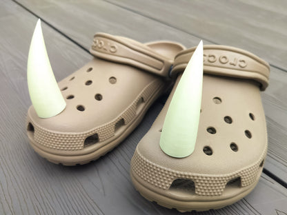 Pair of tan shoes with large glow-in-the-dark 3D printed rhino horn charms attached to the front, placed on a wooden surface.