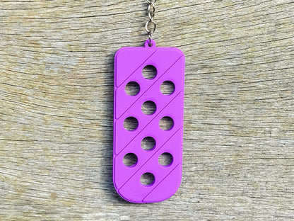 Three PVC keychains in pink, white, and blue with holes designed to hold shoe charms. Each keychain displays a unique set of charms, including candy-themed and colorful glitter charms, showcasing a playful and customizable accessory for charm lovers.