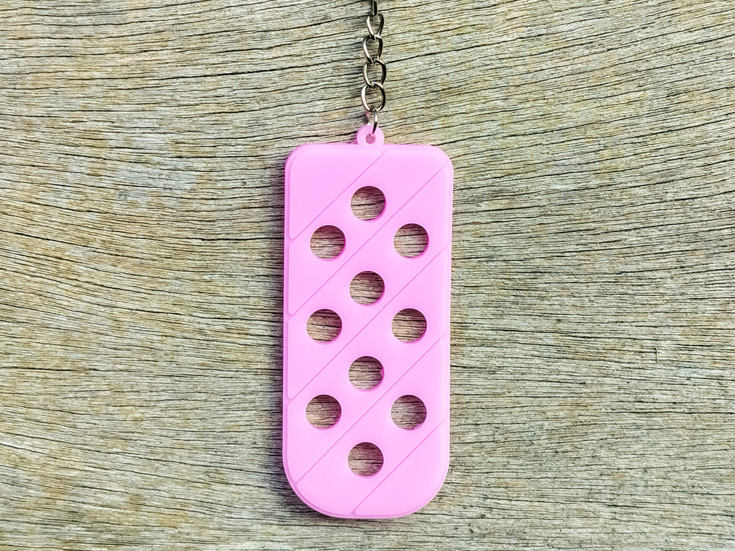 Three PVC keychains in pink, white, and blue with holes designed to hold shoe charms. Each keychain displays a unique set of charms, including candy-themed and colorful glitter charms, showcasing a playful and customizable accessory for charm lovers.