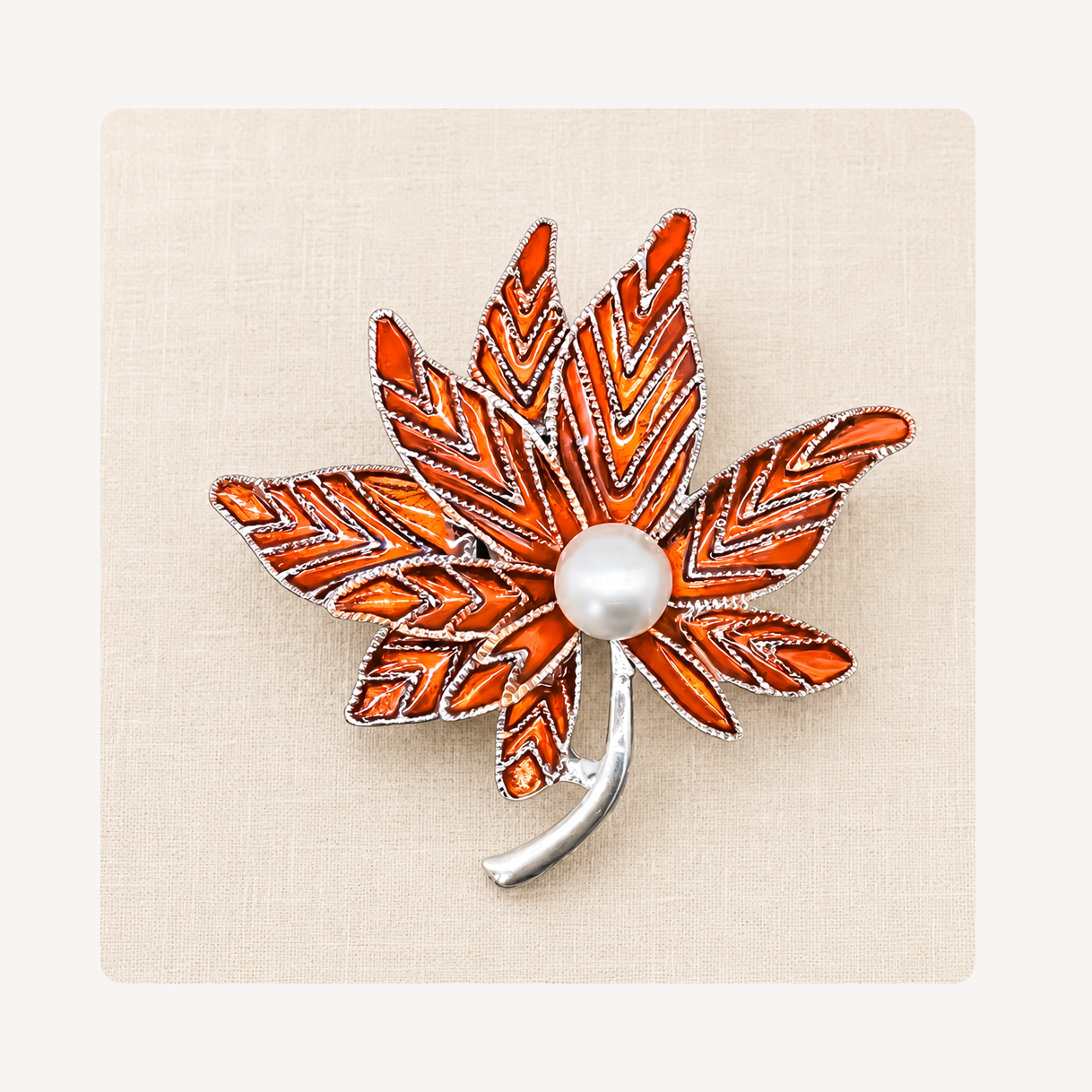 An autumn maple leaf clog charm featuring vibrant orange and red enamel, a white faux-pearl center, and a silver-tone metal outline and stem, displayed on a textured beige background.