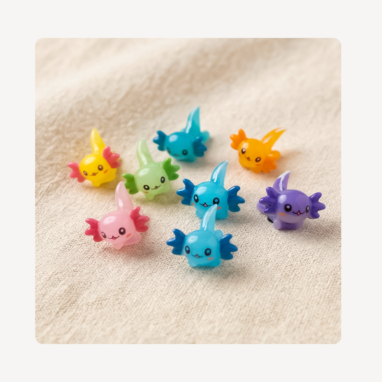 Seven small, cute, cartoonish axolotl clog charms in assorted pastel and bright colors, including pink, yellow, green, blue, orange, and purple, arranged on a textured beige fabric background.