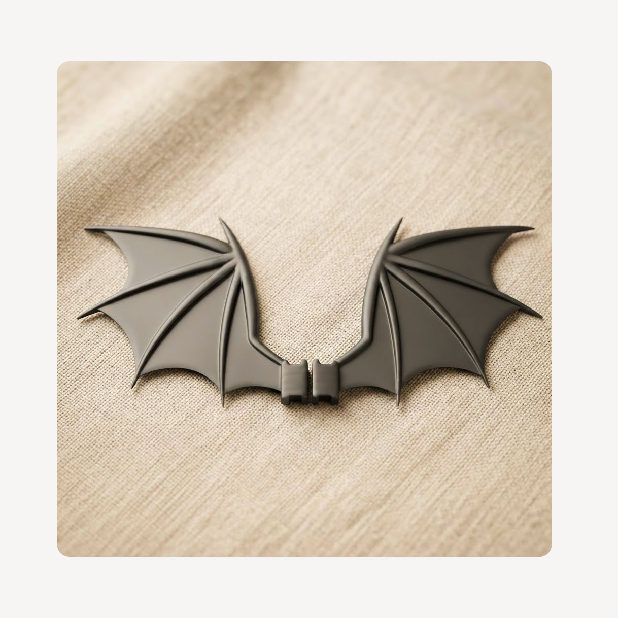 A black bat-wing shaped clog charm displayed on a textured beige fabric background.