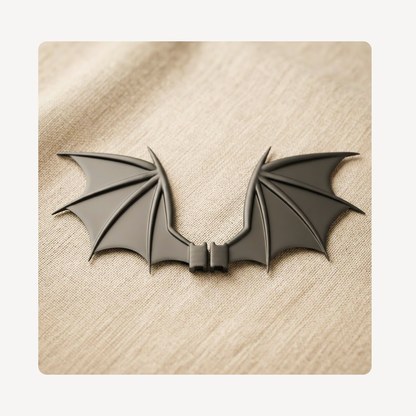 A black bat-wing shaped clog charm displayed on a textured beige fabric background.