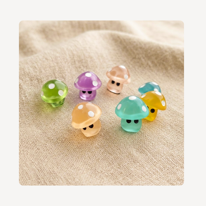 Seven small mushroom-shaped clog charms in pastel colors with white polka dots and cartoon eyes, arranged on a beige fabric background.