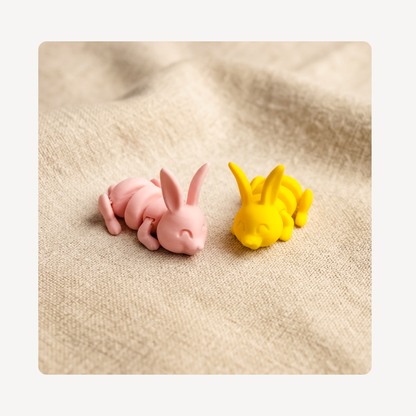 Two small bunny clog charms, one pink and one yellow, placed on a beige textured fabric background.