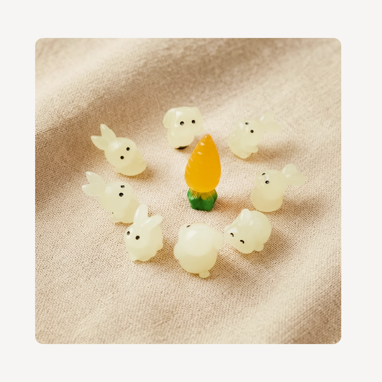 A set of small translucent white bunny clog charms arranged in a circle around a central yellow-orange carrot charm with a green base, displayed on a textured beige fabric background.