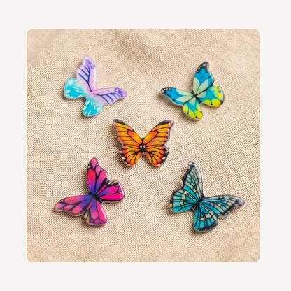 Five colorful butterfly-shaped clog charms arranged on a beige textured fabric background.