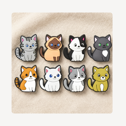 Eight cute cartoon cat clog charms arranged in two rows on a textured beige fabric background. The cats are in various colors including gray, orange, black and white, yellow, and orange and white.