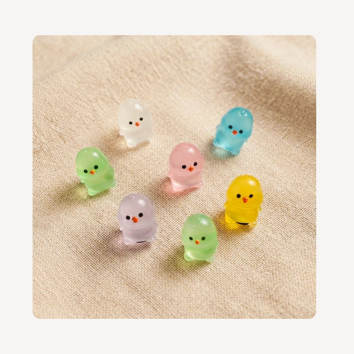 Seven small translucent chicken-shaped clog charms in pastel colors with simple black eyes and orange beaks, arranged on a beige textured fabric background.