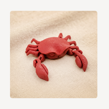 A small red crab clog charm placed on a textured beige fabric background.