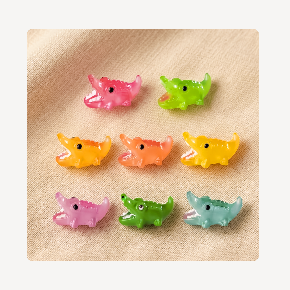 Eight small crocodile-shaped clog charms in assorted pastel and bright colors, arranged in a 3-by-3 grid on a beige textured fabric background.