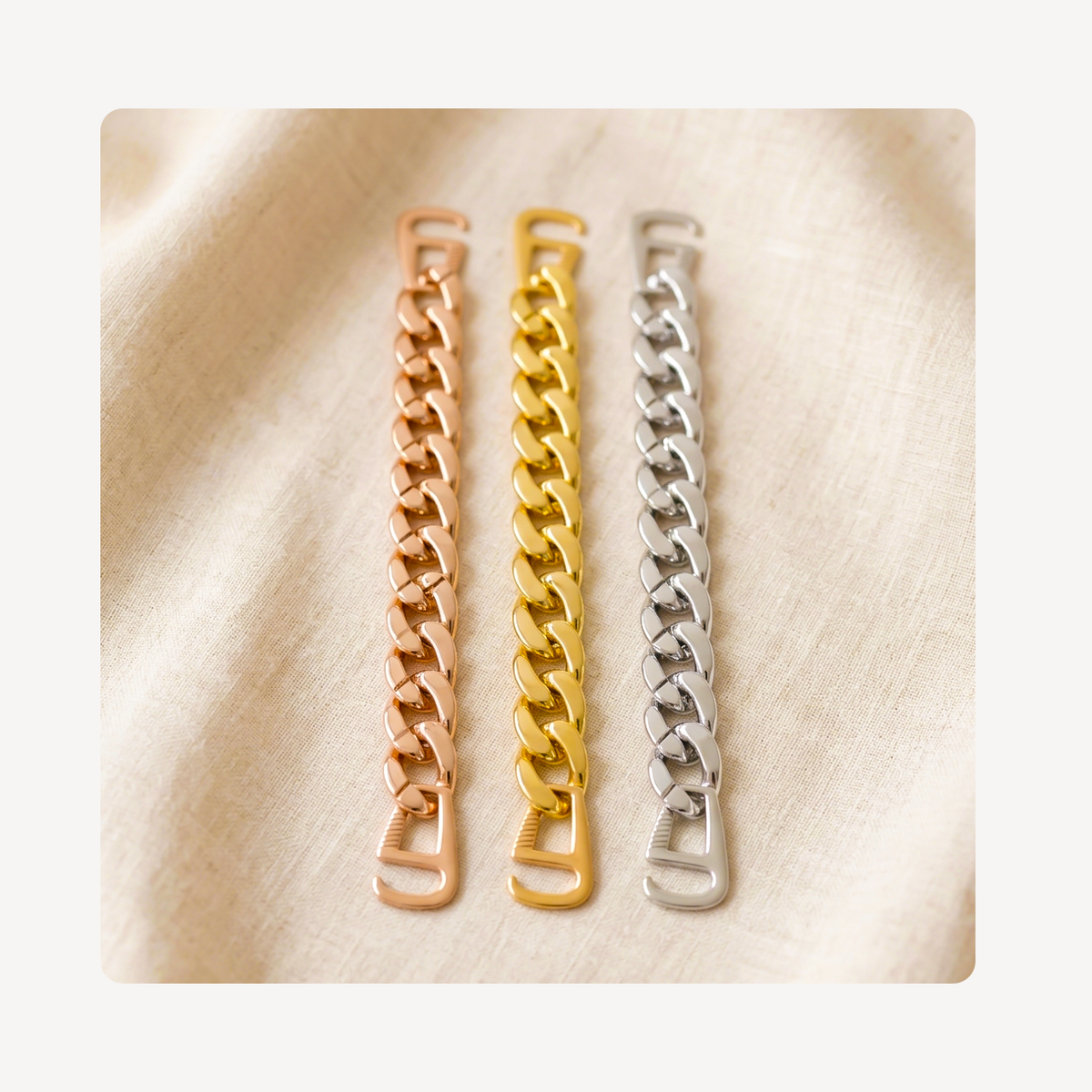 Three curb-link chain clog strap charms in rose gold, yellow gold, and silver, displayed vertically on a textured beige fabric background.