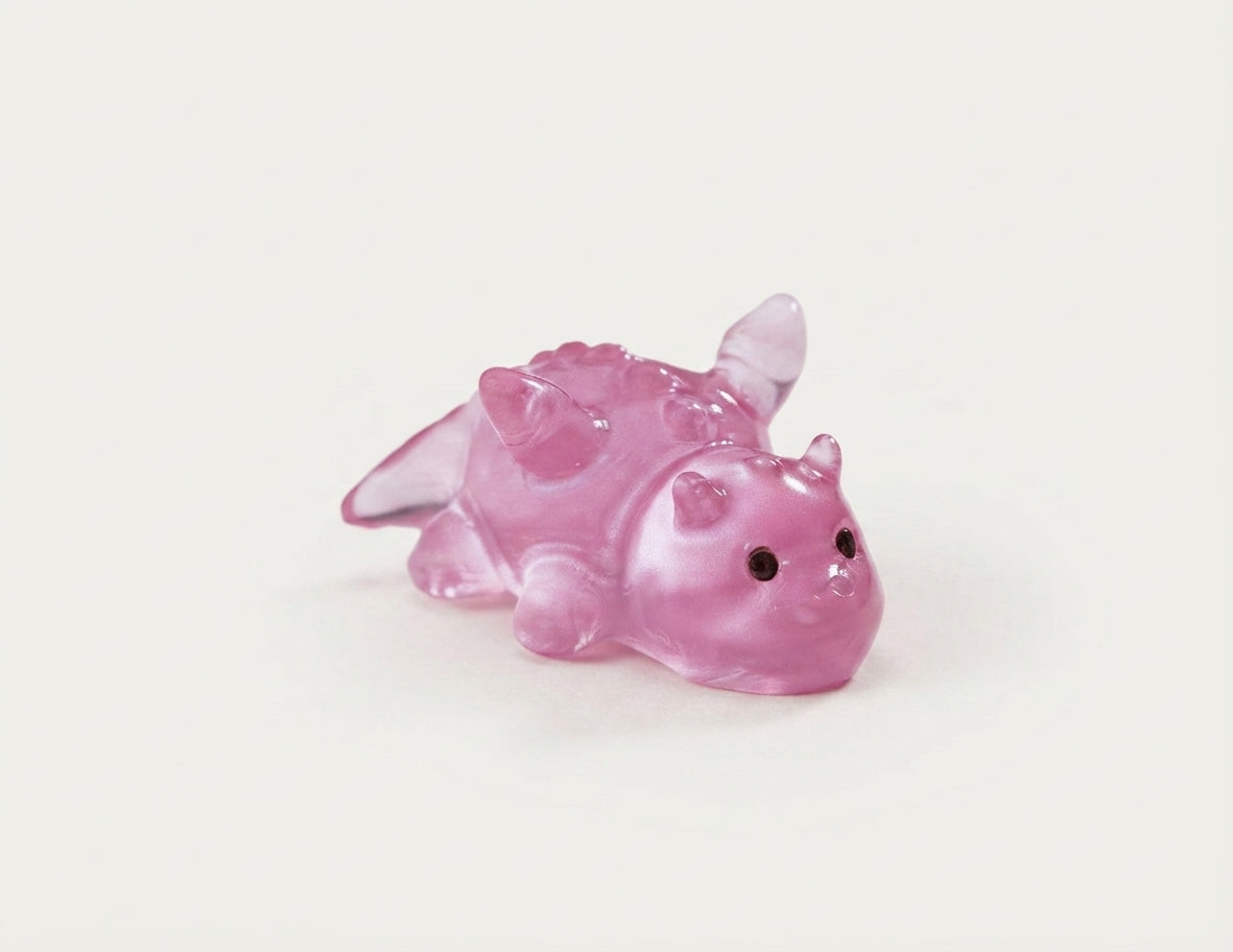 A small translucent pink dragon clog charm with black bead eyes, shown on a plain off-white background.