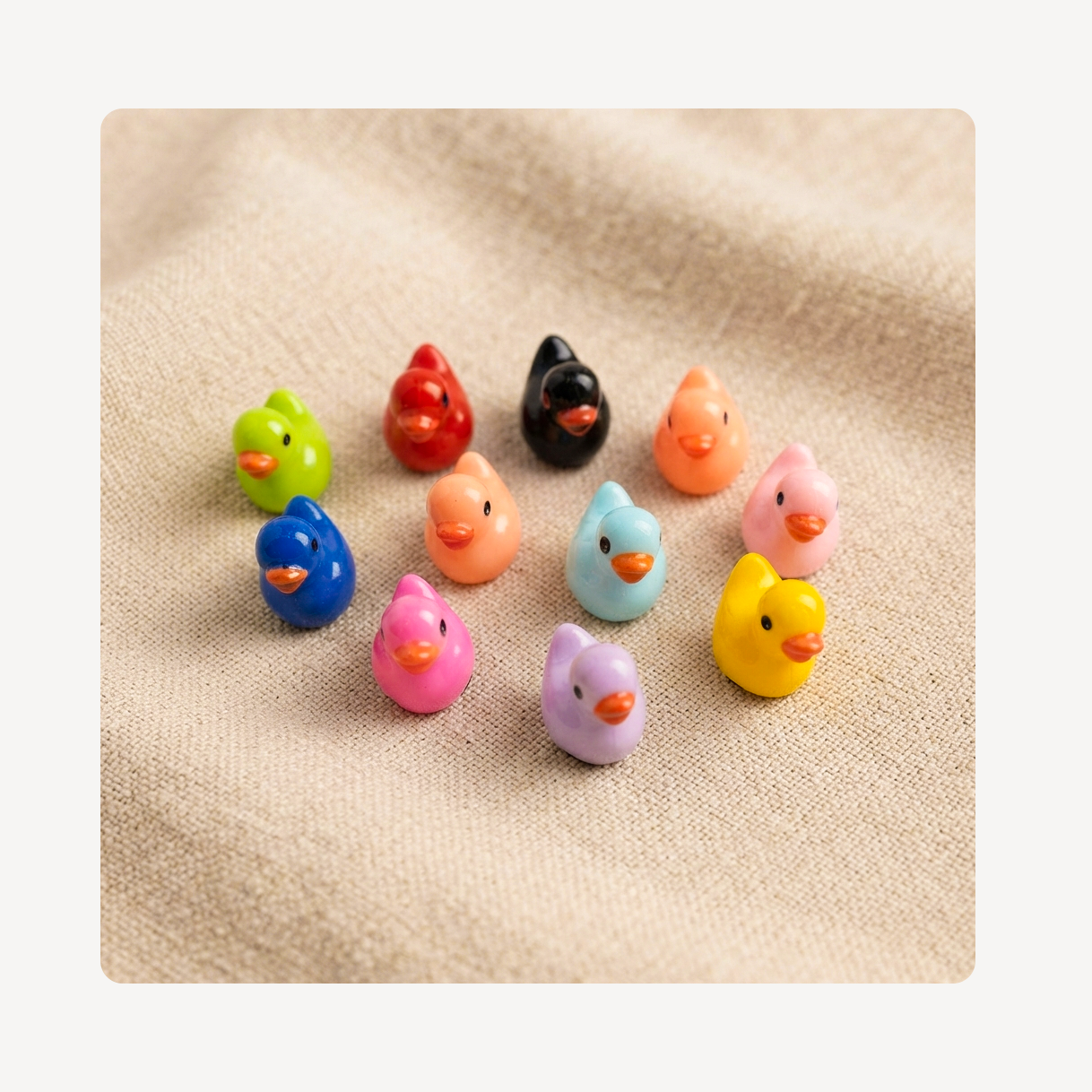 A set of small, colorful duck-shaped clog charms arranged on a textured beige fabric background. The set includes multiple colors: green, red, black, orange, pink, blue, peach, light blue, yellow, and lavender.