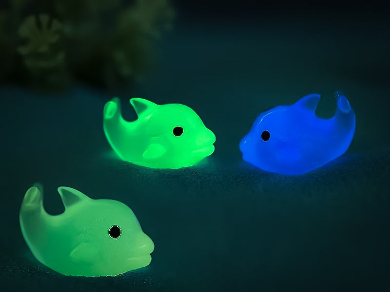Six glow-in-the-dark dolphin charms in various pastel colors, including purple, pink, orange, green, blue, and white, are arranged on a yellow shoes shoe. The dolphins have tiny black eyes and wide grins, giving them a playful and cute appearance.