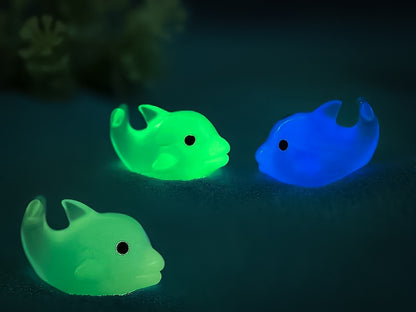 Six glow-in-the-dark dolphin charms in various pastel colors, including purple, pink, orange, green, blue, and white, are arranged on a yellow shoes shoe. The dolphins have tiny black eyes and wide grins, giving them a playful and cute appearance.