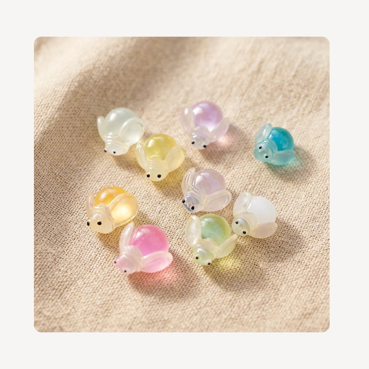 Nine small translucent firefly-shaped clog charms arranged on a beige textured fabric background. The charms come in pastel colors including white, pink, yellow, green, purple, and blue, each with small black bead eyes.