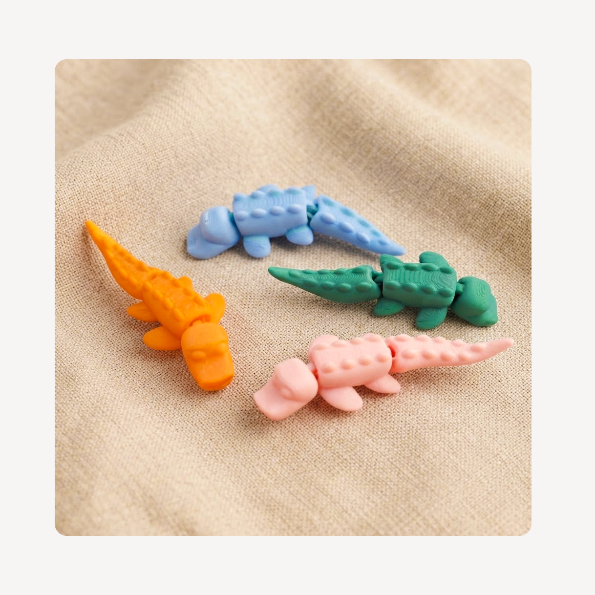 Four small crocodile-shaped clog charms in orange, light blue, green, and pink, arranged on a beige textured fabric background.