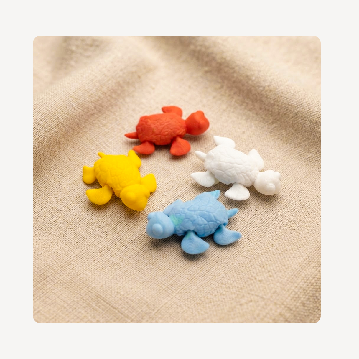 Four small sea turtle clog charms in orange, yellow, white, and light blue, arranged on a beige textured fabric background.
