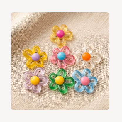 Six small translucent flower-shaped clog charms in pastel colors, arranged on a beige fabric background. The flowers have layered petal designs with centers in pink, purple, blue, orange, yellow, green, and light blue.