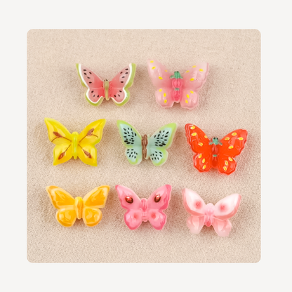 Six colorful butterfly-shaped clog charms arranged in a 3-by-2 grid on a textured beige fabric background.