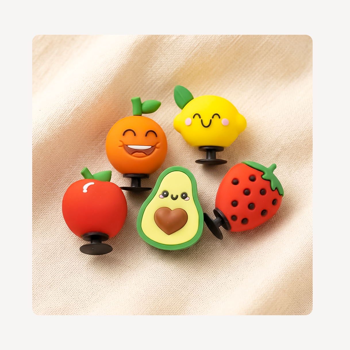 Five fruit-shaped clog charms arranged on a beige fabric background.