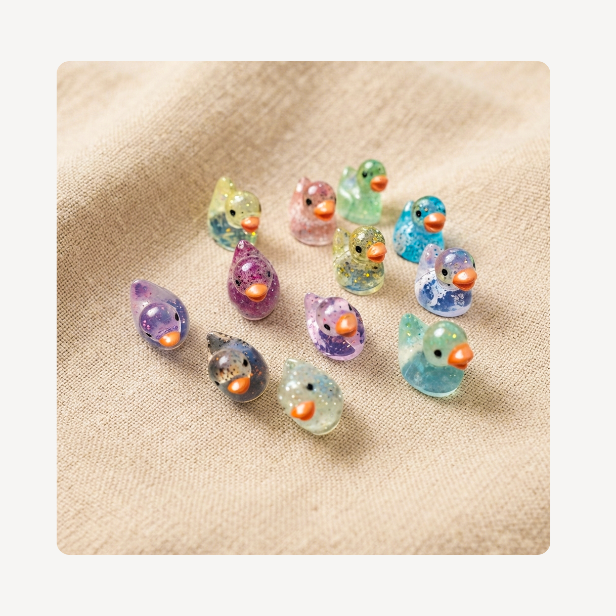 A group of small translucent bird-shaped clog charms in pastel colors with glitter and orange beaks, arranged on a beige fabric background.