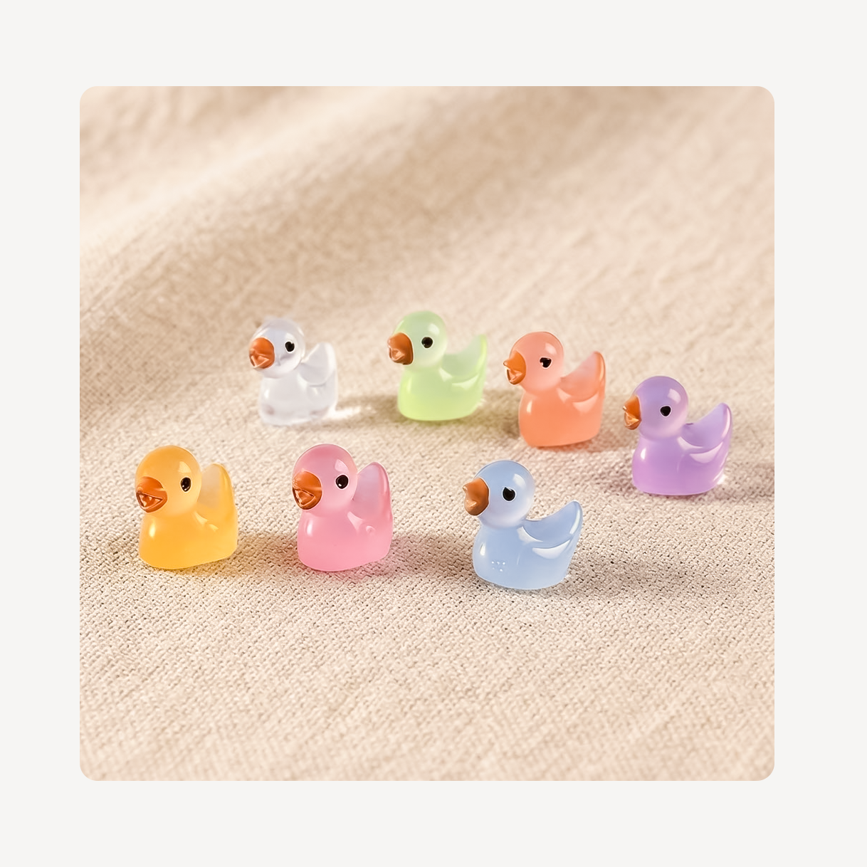 Seven small translucent duck-shaped clog charms in pastel colors including yellow, pink, light blue, orange, green, purple, and white, arranged on a beige textured fabric background.