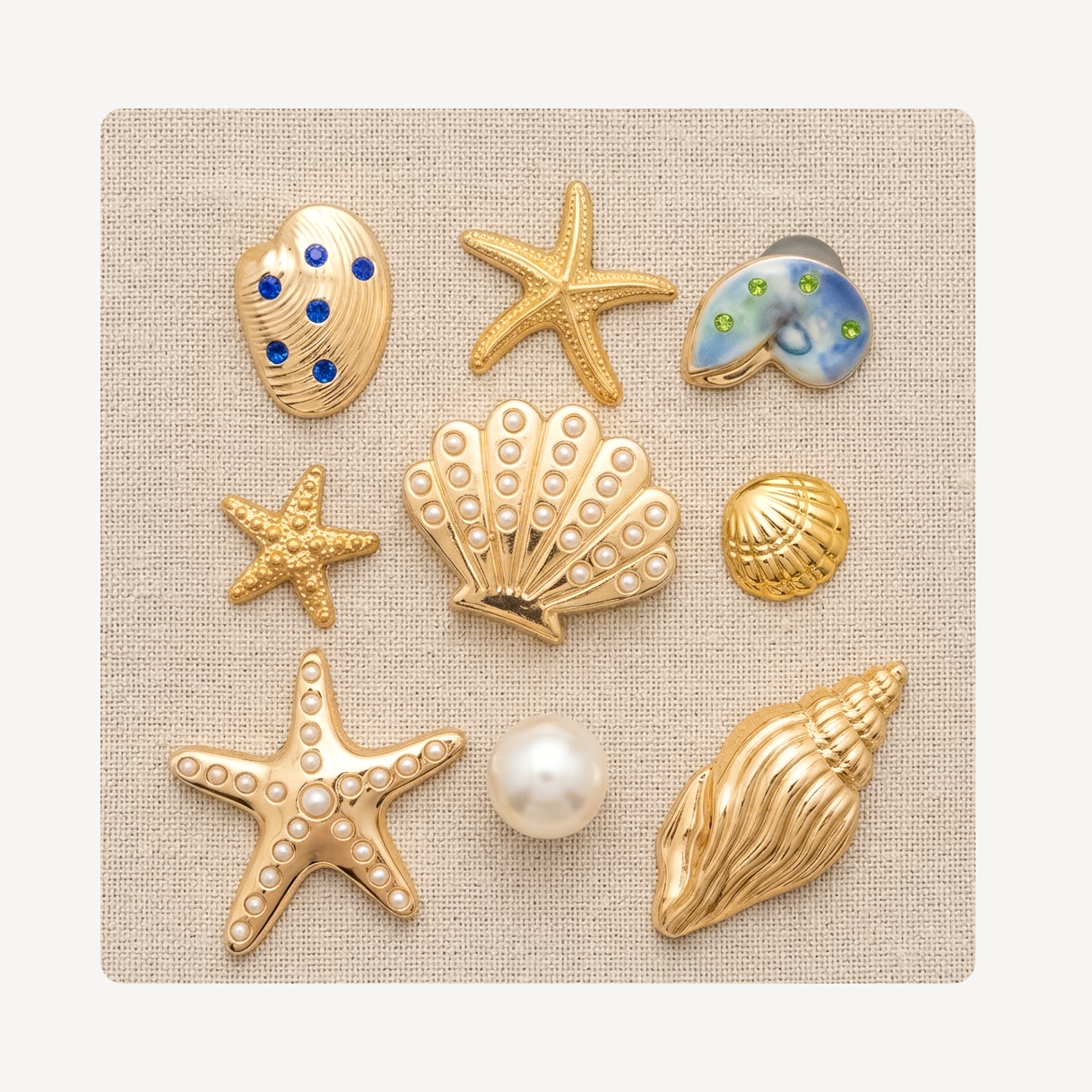 Nine seashell and starfish-shaped clog charms arranged on a square beige fabric background. The set includes gold-tone starfish and shell charms with faux pearls, blue and green stone accents, and one larger gold conch shell.
