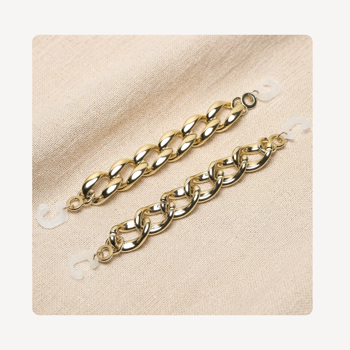 Two gold-toned curb chain link clog chains displayed on a textured beige fabric background.