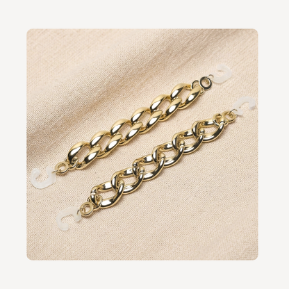 Two gold-toned curb chain link clog chains displayed on a textured beige fabric background.