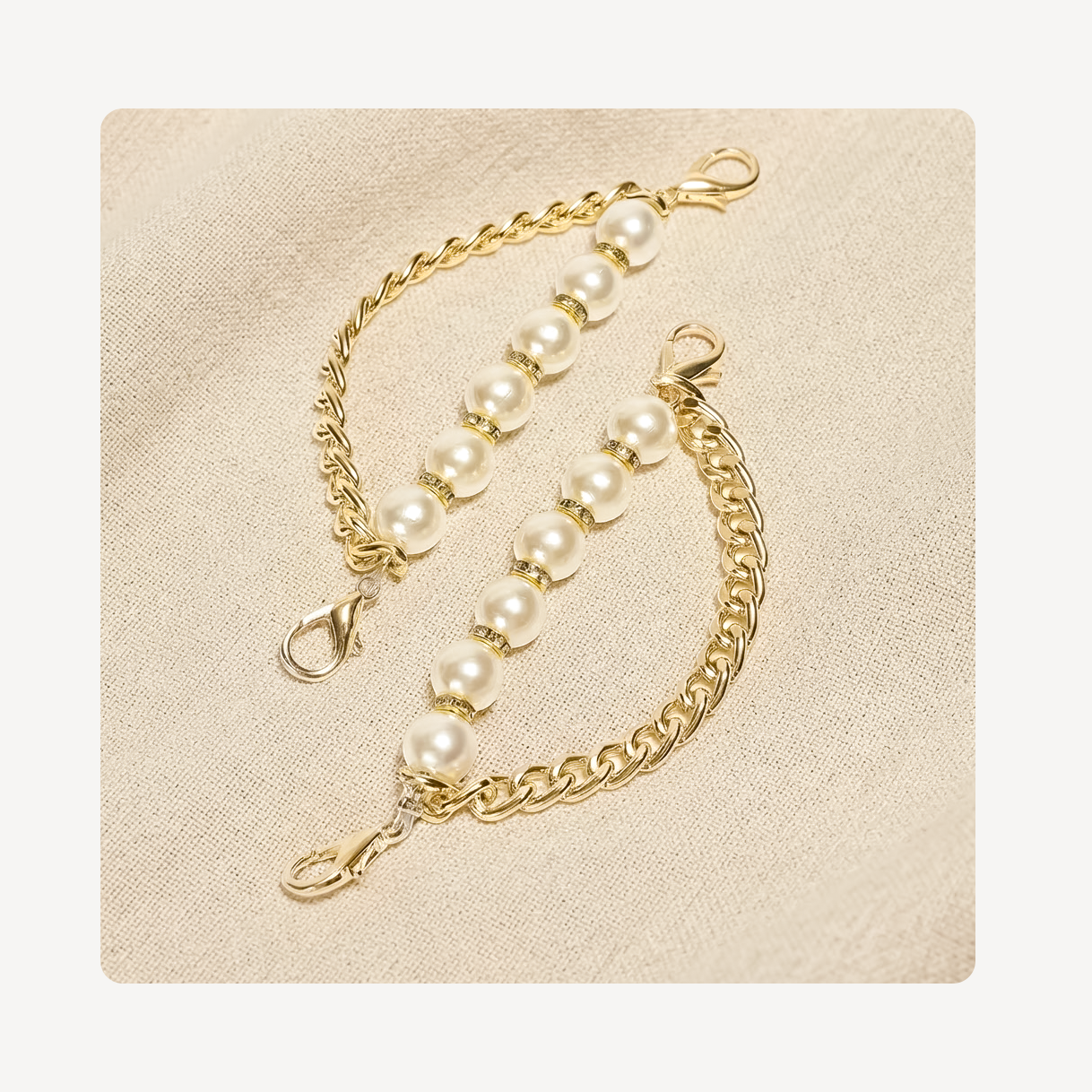 A pair of gold shoe chains with white pearl beads and lobster clasp connectors, displayed on a textured beige fabric background.