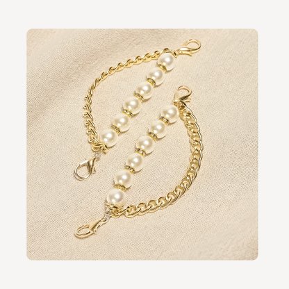 A pair of gold shoe chains with white pearl beads and lobster clasp connectors, displayed on a textured beige fabric background.
