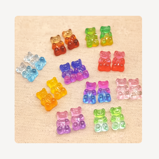 Twelve pairs of colorful translucent gummy bear clog charms arranged on a beige textured fabric background.