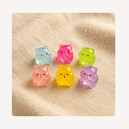 Six small translucent hamster-shaped clog charms in pastel colors, arranged on a beige textured fabric background.