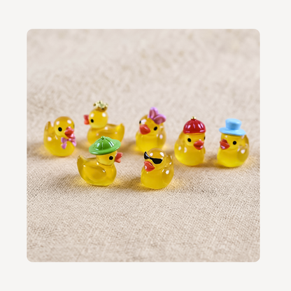 A group of small translucent yellow duck clog charms with colorful hats and accessories, arranged on a beige textured fabric background.