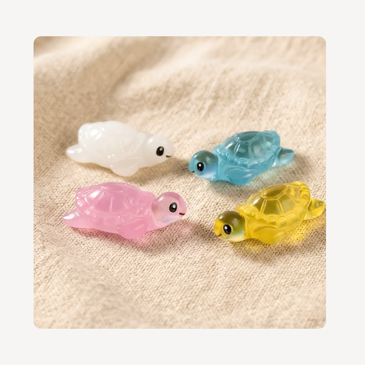 Four small translucent turtle clog charms in white, blue, pink, and yellow, arranged on a beige textured fabric background.