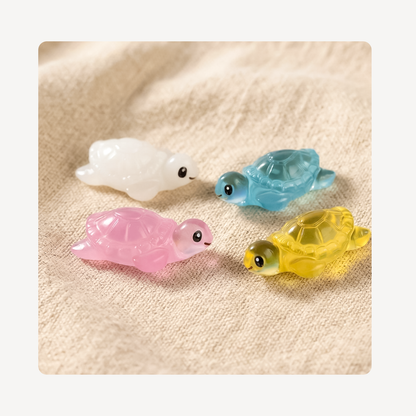 Four small translucent turtle clog charms in white, blue, pink, and yellow, arranged on a beige textured fabric background.