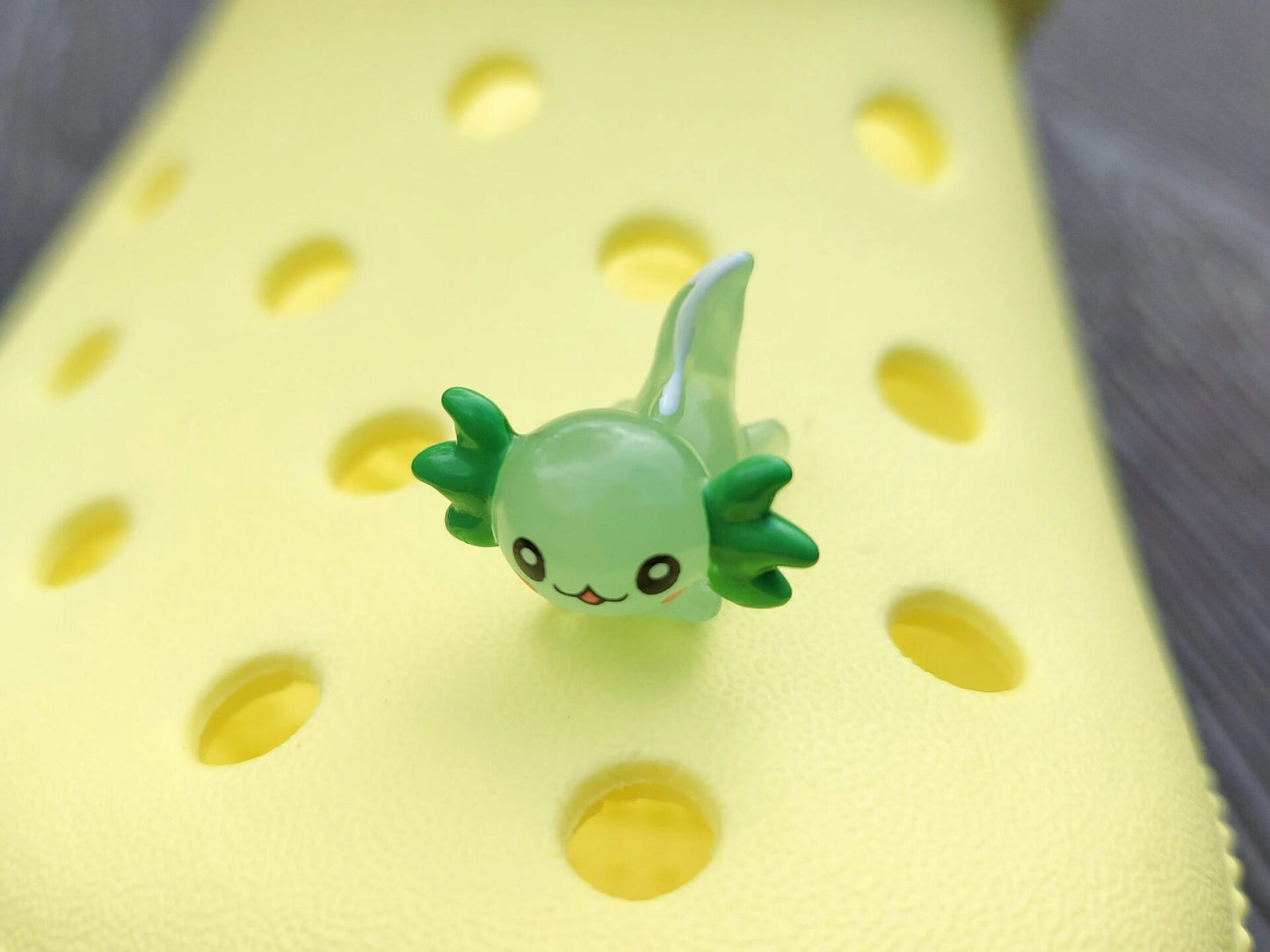 Colorful axolotl charms on a pair of yellow shoes shoes. The axolotls are blue, purple, green, orange, yellow and pink and have cute, smiling faces.