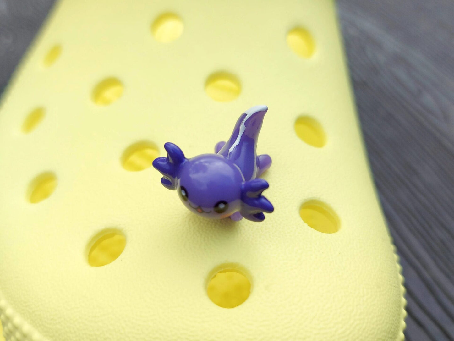 Colorful axolotl charms on a pair of yellow shoes shoes. The axolotls are blue, purple, green, orange, yellow and pink and have cute, smiling faces.