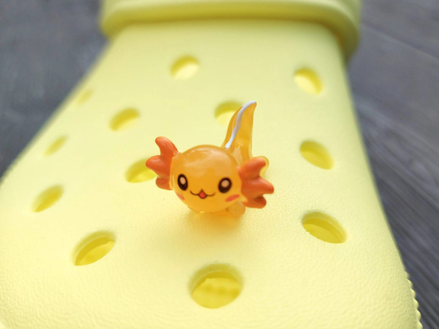 Colorful axolotl charms on a pair of yellow shoes shoes. The axolotls are blue, purple, green, orange, yellow and pink and have cute, smiling faces.