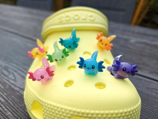 Colorful axolotl charms on a pair of yellow shoes shoes. The axolotls are blue, purple, green, orange, yellow and pink and have cute, smiling faces.