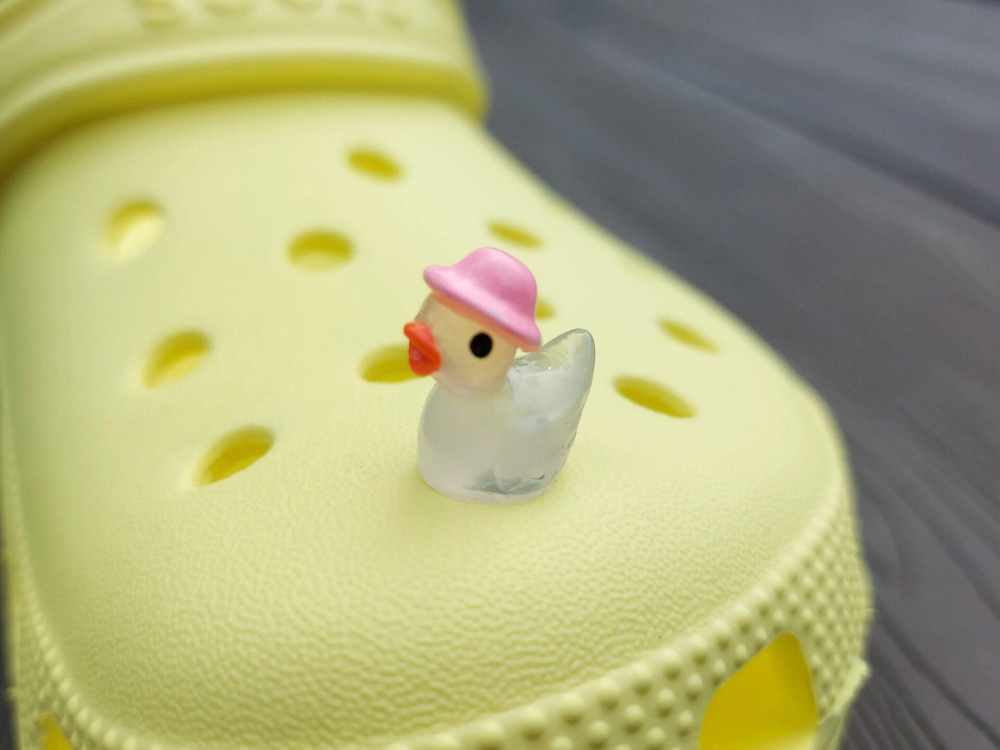 Glow in the dark duck charms wearing bucket hats on a yellow shoes shoe. These colorful charms are available in pink, white, blue, green, yellow, turquoise, peach and purple. The hats all have different colors.